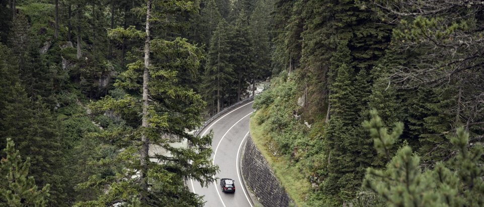 Elbil eller plug in hybrid - bil kører på kurvet vej i skov