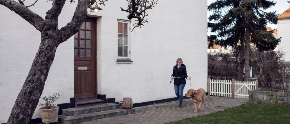 Kvinde med sin hund foran stor villa 