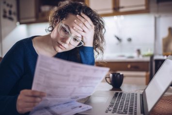 Kvinde der ser bekymret på computer og papirer