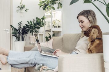 Ung kvinde kigger computer i sofa