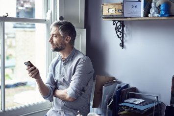 Mand med telefon i hånden kigger ud af vinduet, mens han smiler