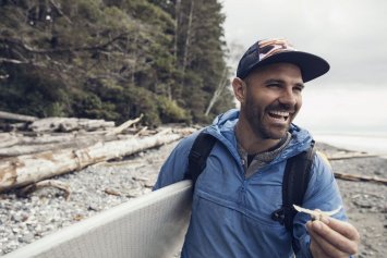 Mand der smiler med et surf board i hånden