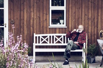 Illustrativt billede, der viser en ælde mand foran et rødt sommerhus i træ
